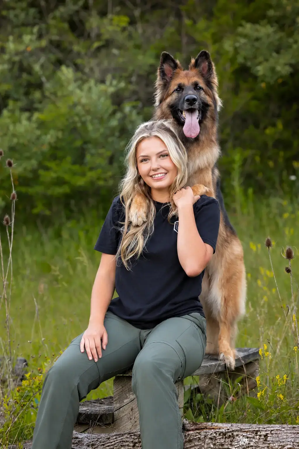 Alexis Bissett smiling with a long-haired German Shepherd resting its paws on her shoulder